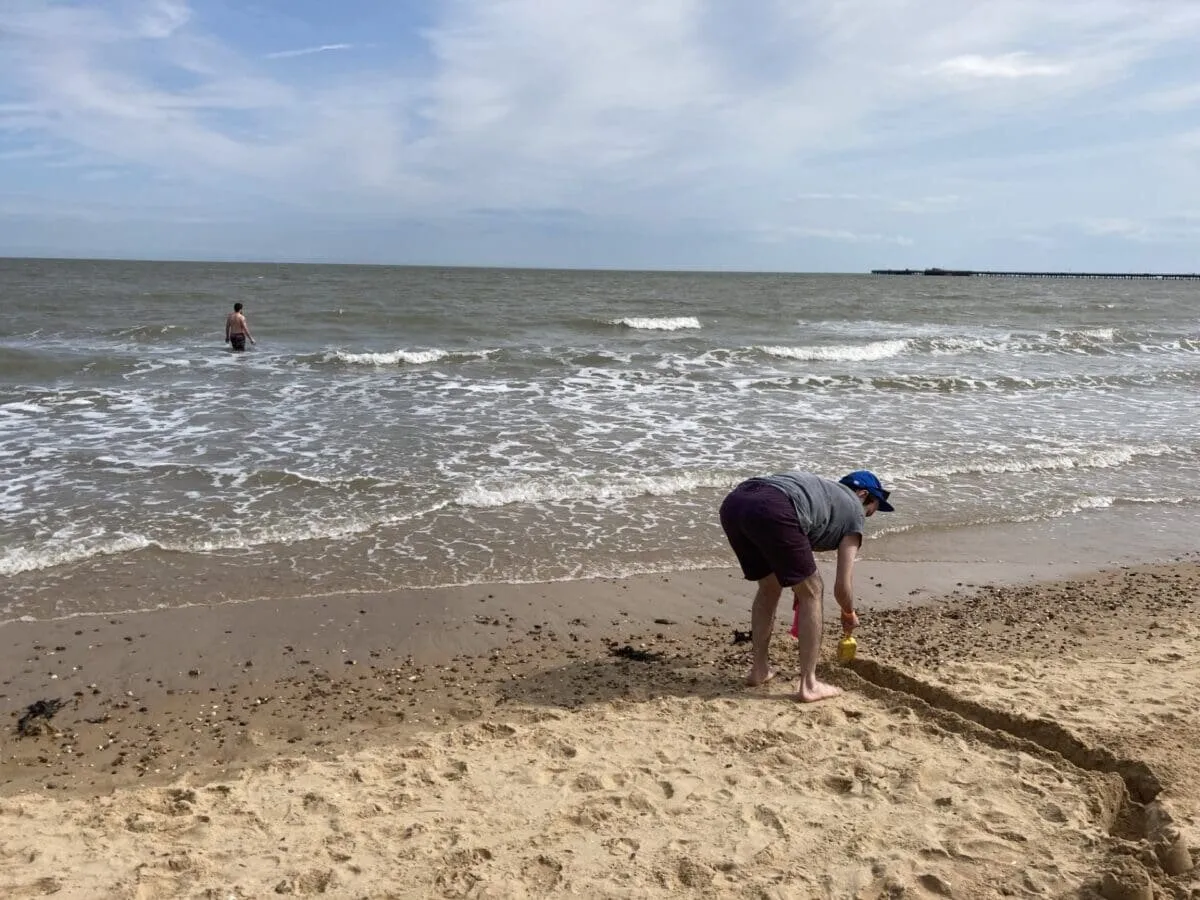 A child digging in the sand at the water’s edge on a calm beach, on a RAGS coach trip to Walton-on-the-Naze