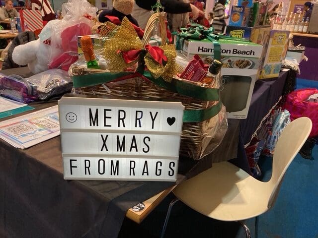 Christmas gift hamper beside a light-box sign reading Merry Xmas from RAGS