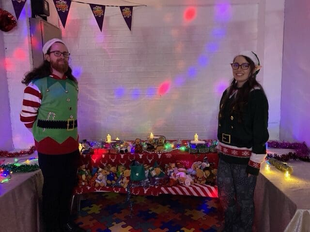 Two volunteers in elf costumes standing by a RAGS Christmas party display