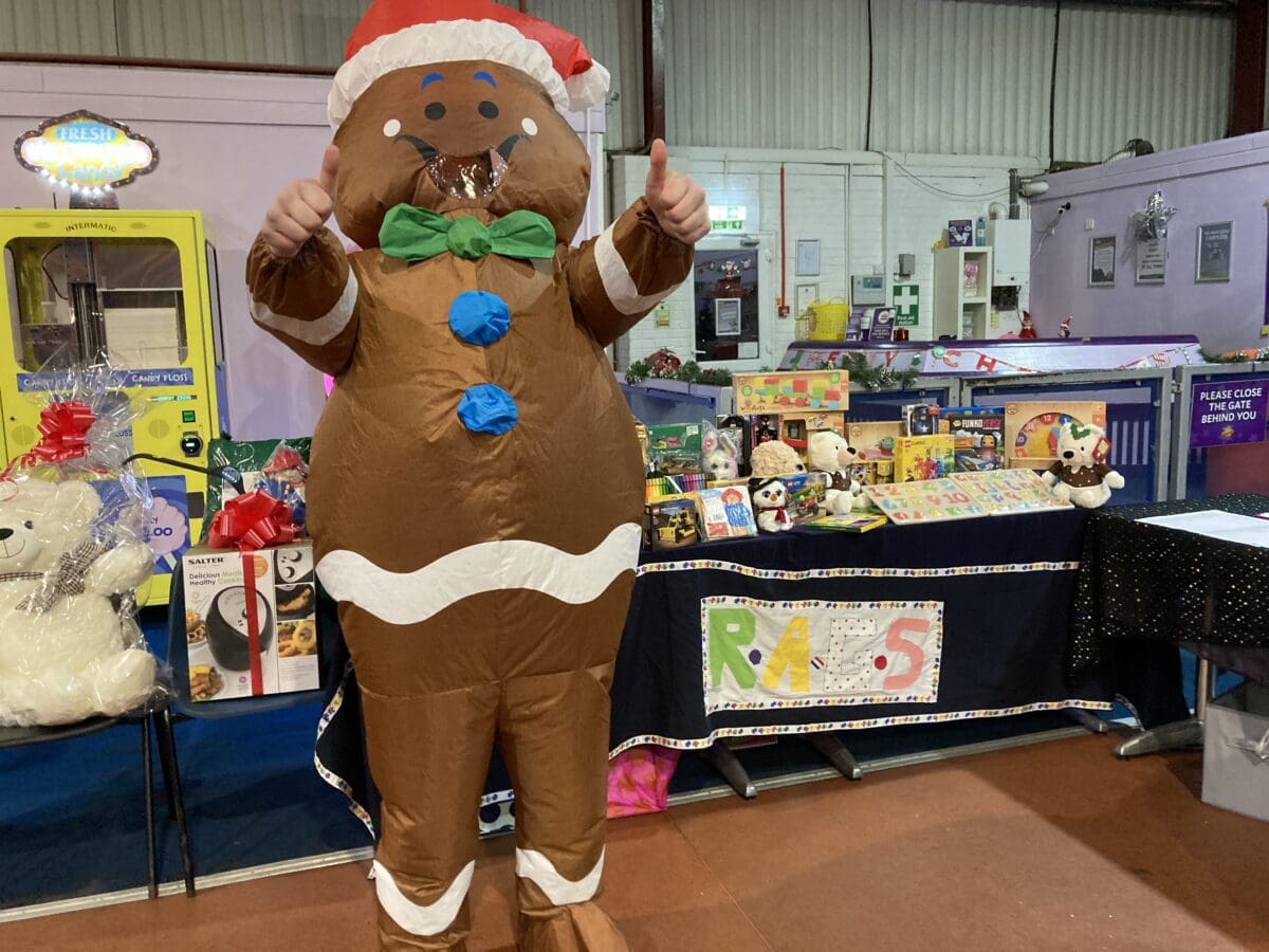 Person in a gingerbread man costume giving a thumbs up at a RAGS Christmas event