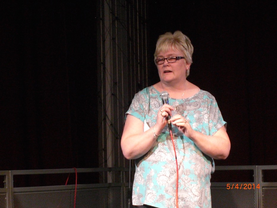 Woman speaking into a microphone on stage at a RAGS event, 2014