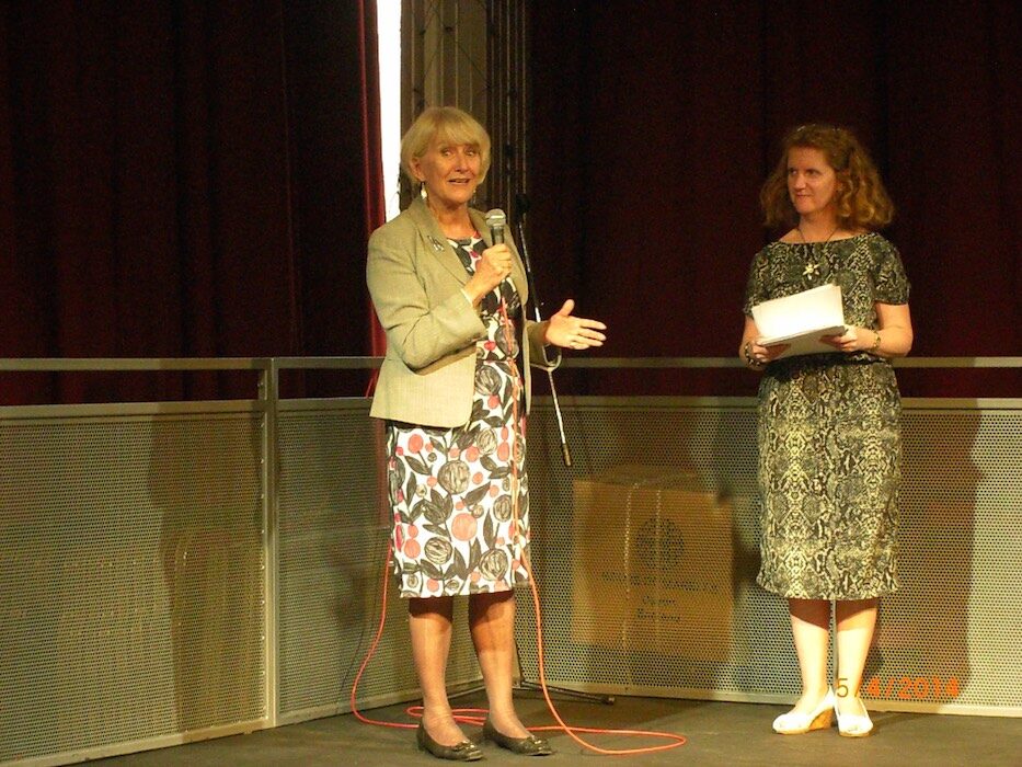 Woman speaking on stage at a RAGS theatre event, 2014