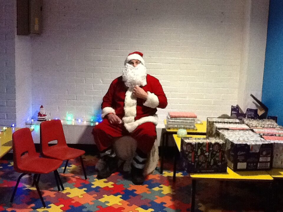 Father Christmas seated beside wrapped presents at RAGS Christmas party