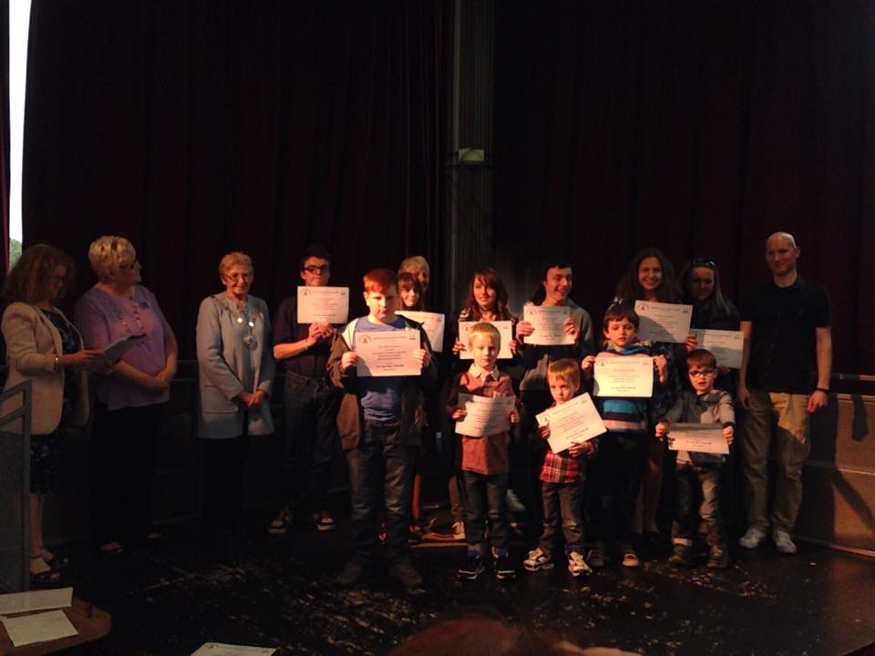 Children and young people on stage holding certificates at a RAGS awards ceremony