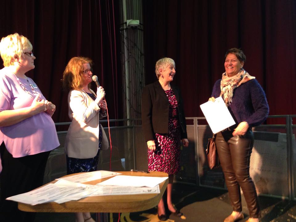 Four women on stage at a RAGS event, one speaking into a microphone