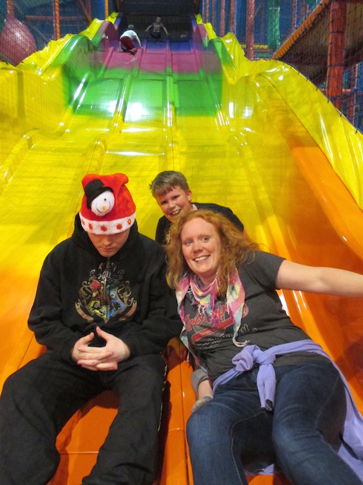 Family sliding down a slide together at a soft play centre, 2014