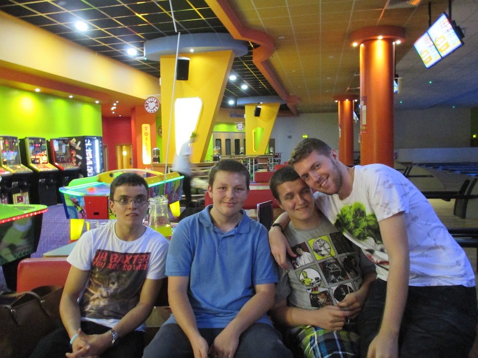 Group of four young men smiling together in a bowling alley lounge, 2014