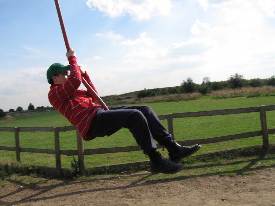 Boy swinging on a rope swing beside a countryside fence, 2014