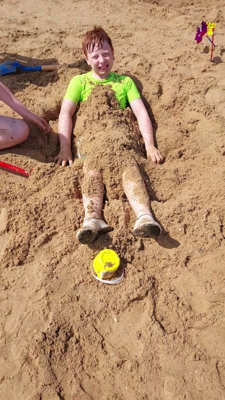 A child buried in the sand for fun on the beach at Walton-on-the-Naze